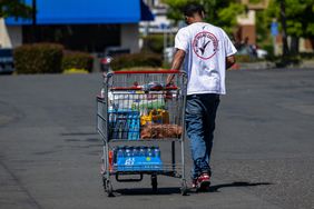 A person pushes a cart filled with groceries in an outdoor parking lot