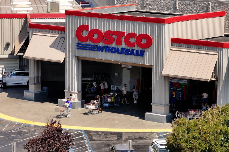 An aerial view of a Costco store, showing the Costco logo and customers exiting the building with shopping carts.