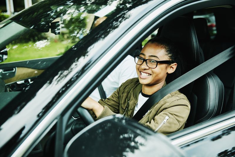 A teen in glasses smiles while driving a car