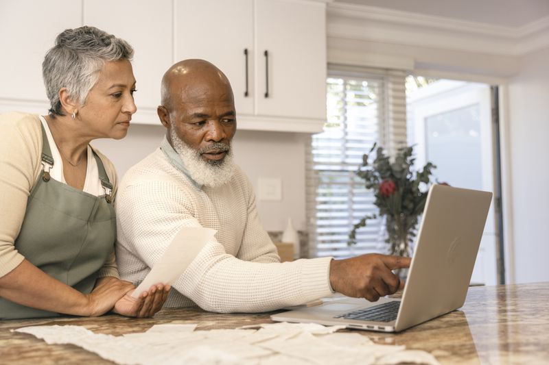 Couple in their 50s or 60s in their kitchen and looking at mortgage rates on a laptop