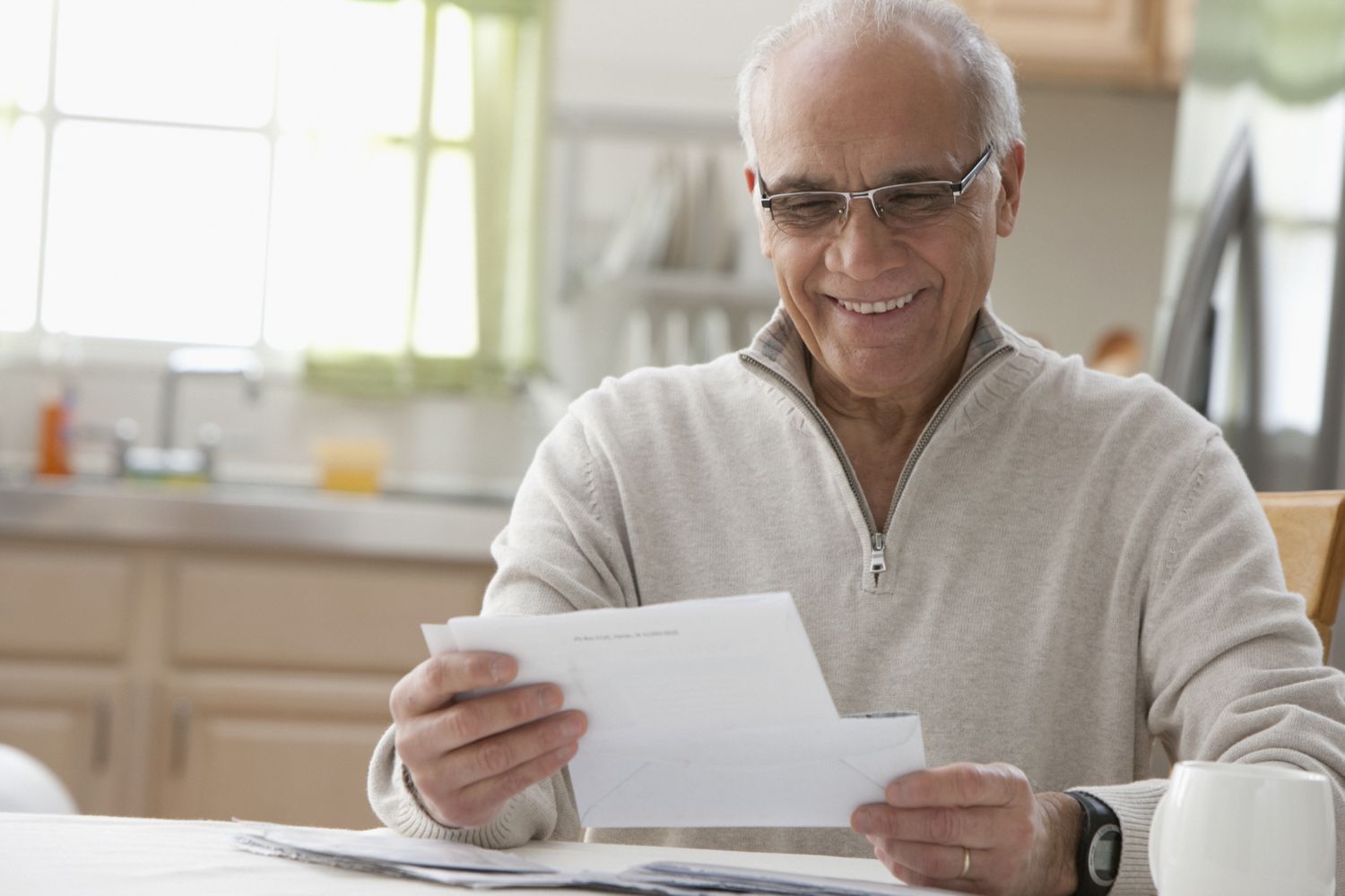 Man sitting at a kitchen table looking at a piece of mail.