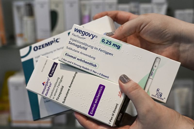 A person holds prescription medication boxes for Wegovy, Ozempic, and Mounjaro at a pharmacy.