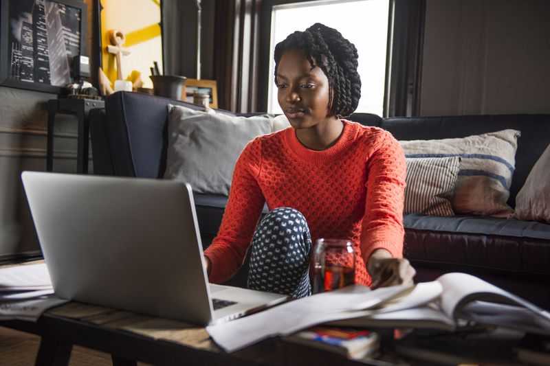 Woman in her apartment, reading on her computer about the hidden costs of owning a home
