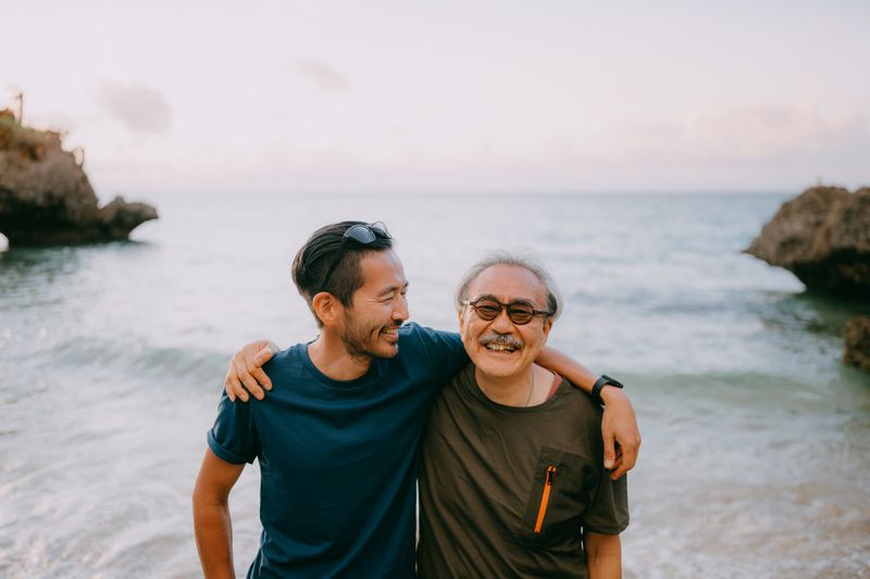 Senior father and adult son hugging and smiling on a beach