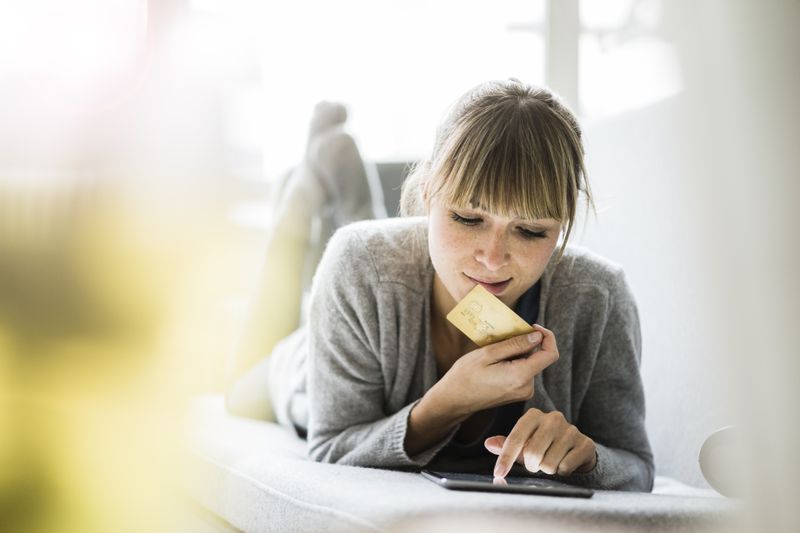 Woman holds a credit card and uses a device.