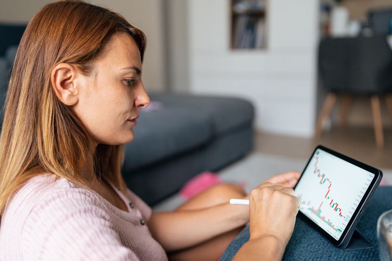 Female trader sitting on a couch and looking at a chart on a tablet