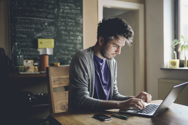Young man working at home, freelancer, designer or writer, checking e-mails or typing on the laptop