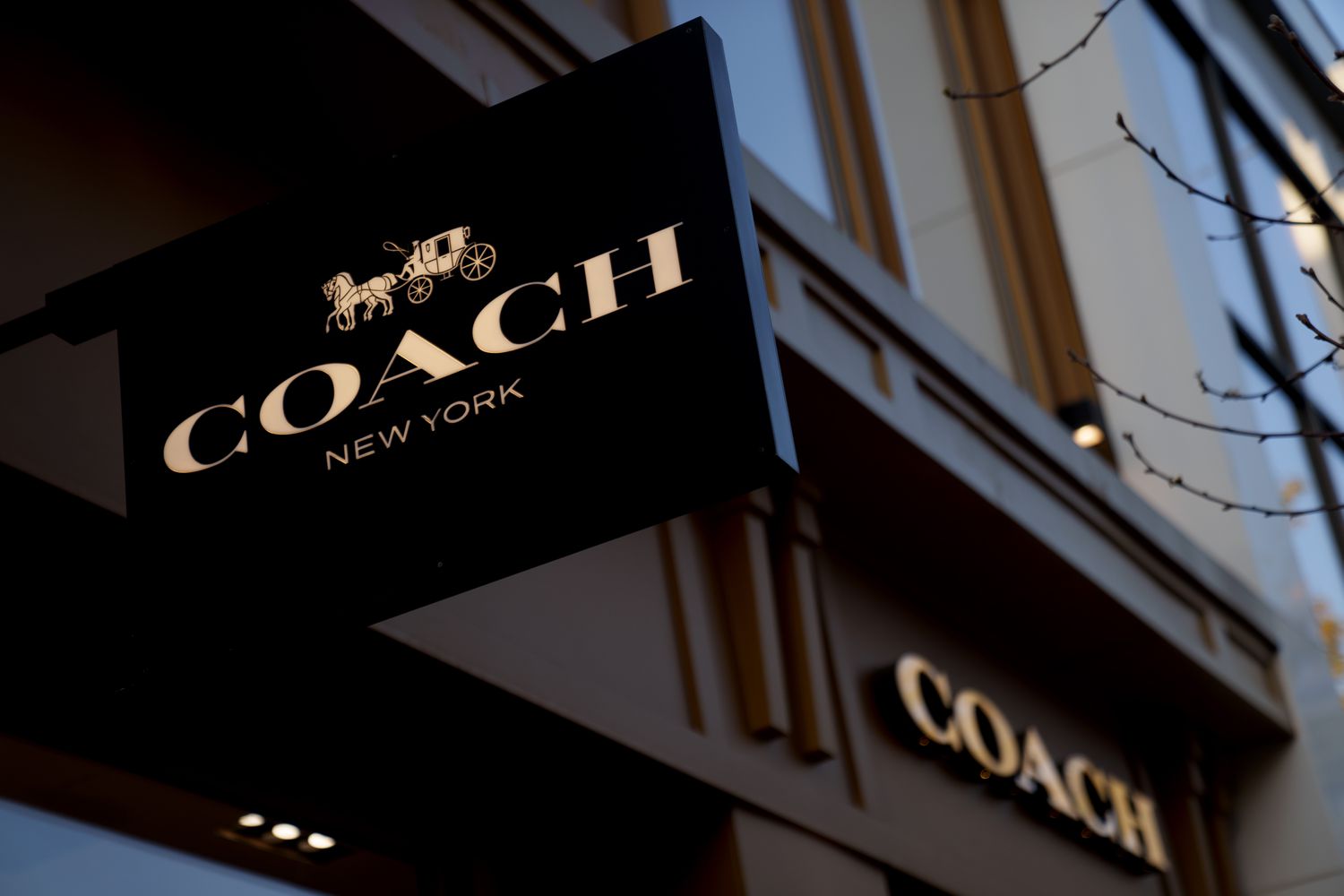 The Coach logo is seen on a black sign hanging above a Coach store.