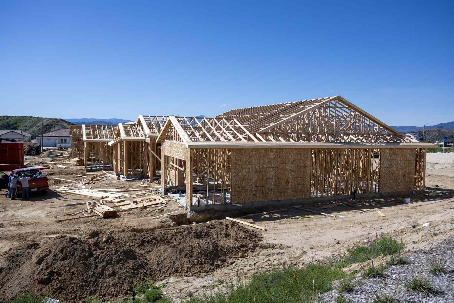 Wood frames of under-construction houses are seen in front of a blue sky.