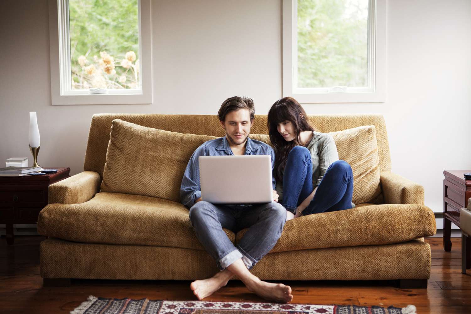 A man and a woman sit on a couch looking at a laptop