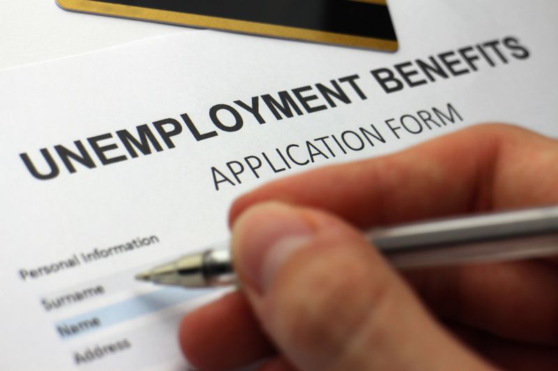 Close up of a hand holding a pen filling out unemployment paperwork to receive unemployment benefits.