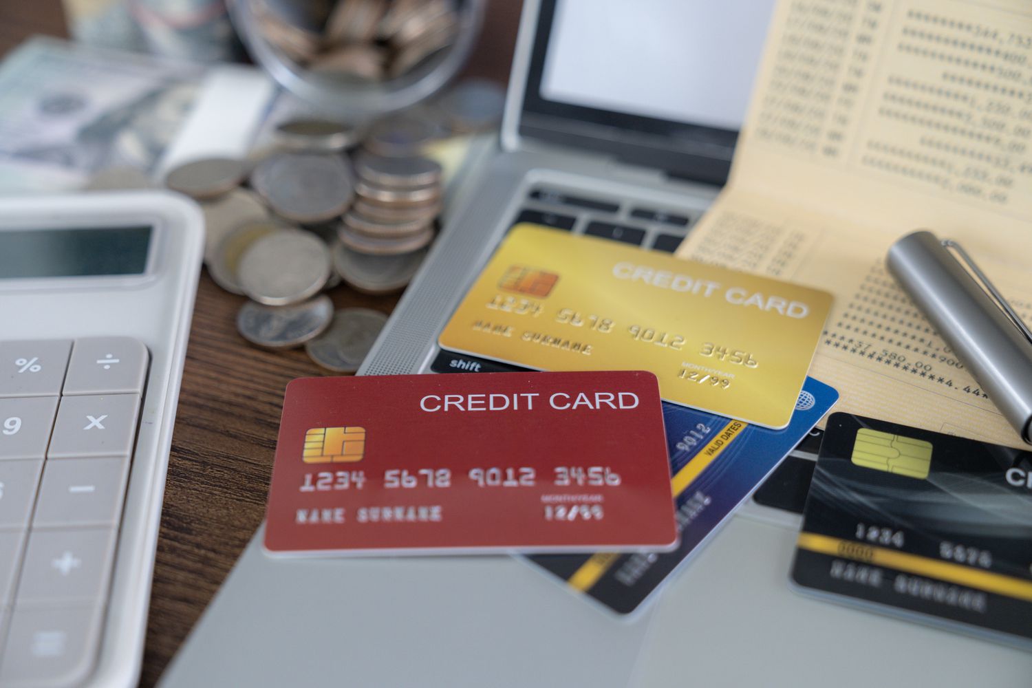credit card stack on the table with calculator, cash, coins, and computer and bills strewn about