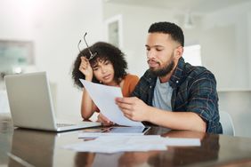Young couple sitting at their dining table and looking at a mortgage document and rates on a laptop