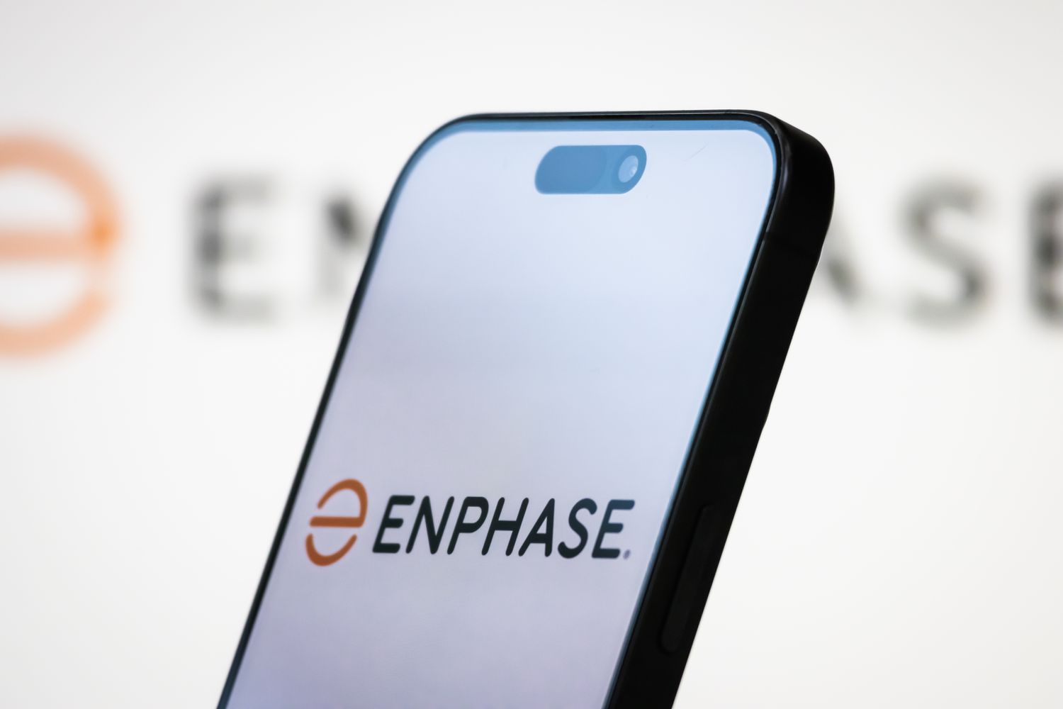 The logo of Enphase Energy, Inc. is displayed on a smartphone screen, with the company's branding in the background