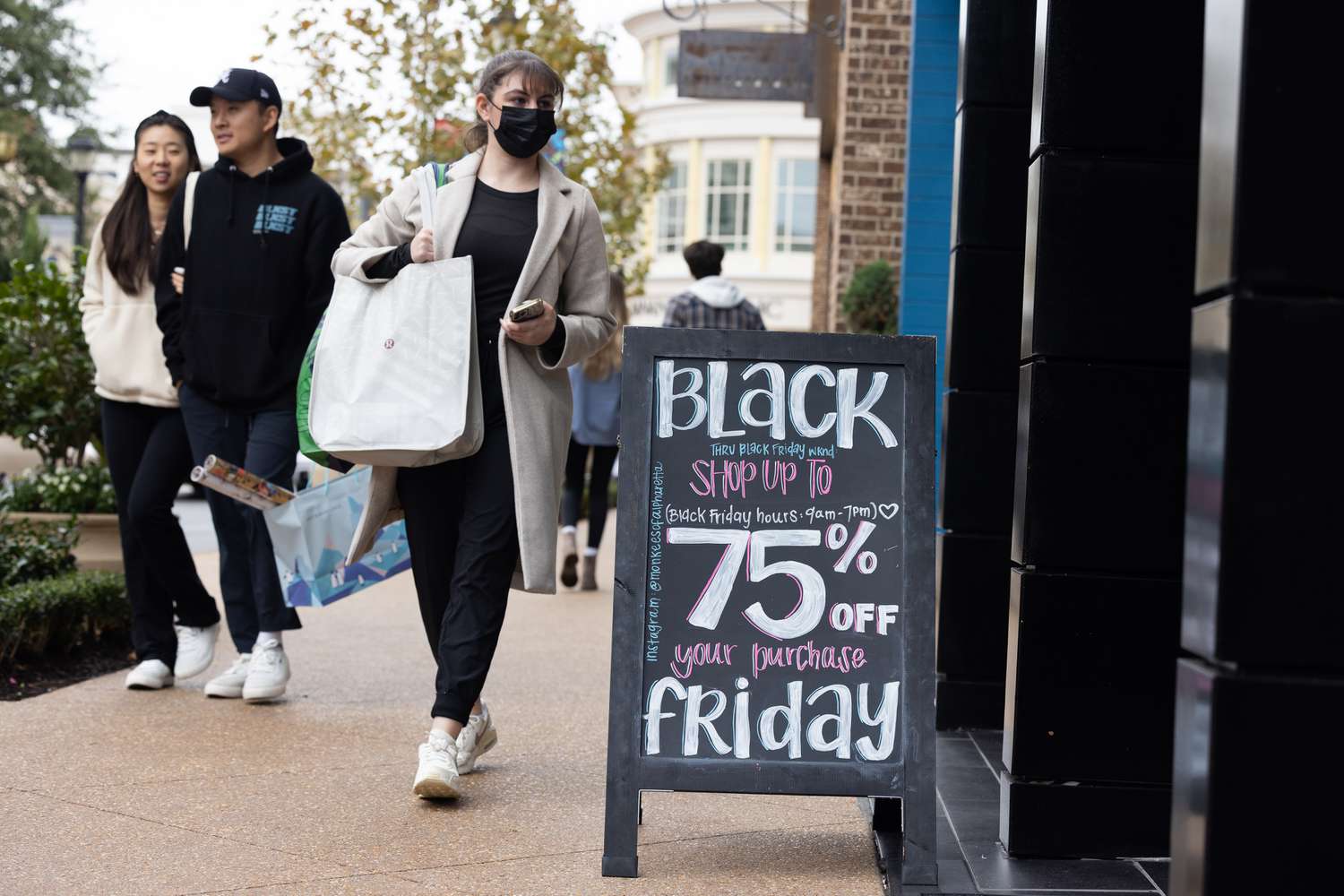 Three people walking down the street with a sign in the foreground promoting a Black Friday sale.