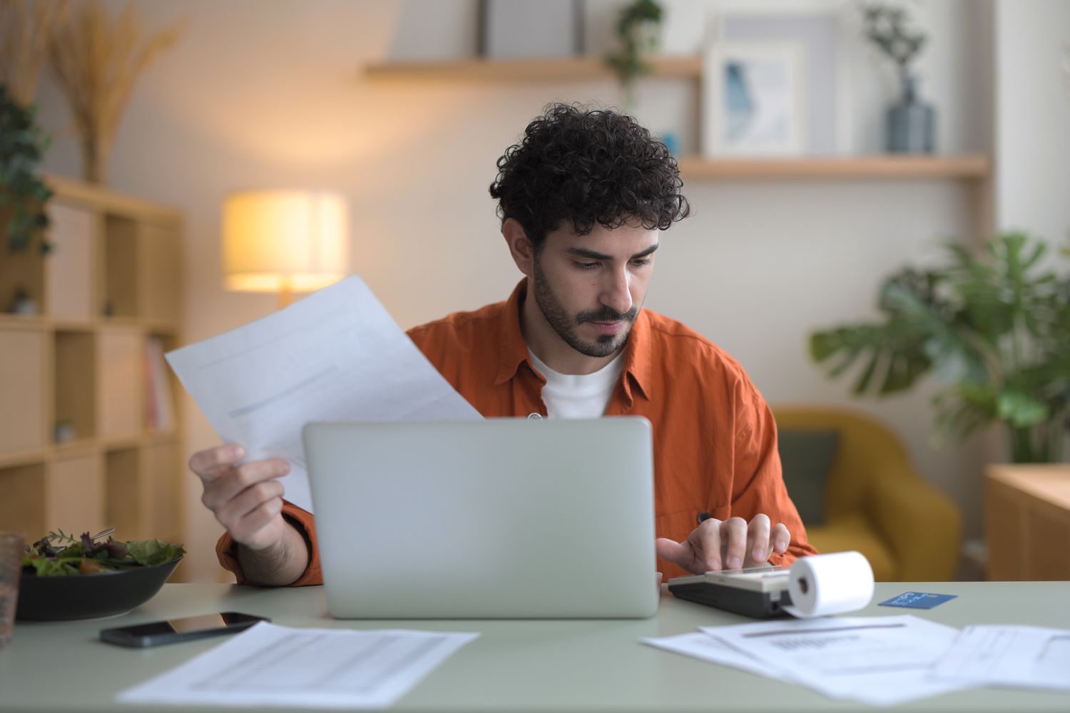 Young adult with curly hair does their taxes on a laptop while sitting at a table.