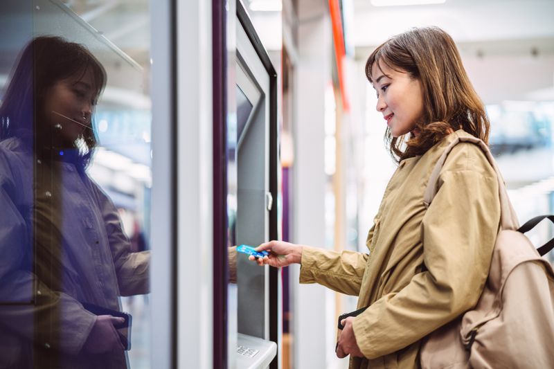 A young woman inserts a bank card into an automatic cash machine. 