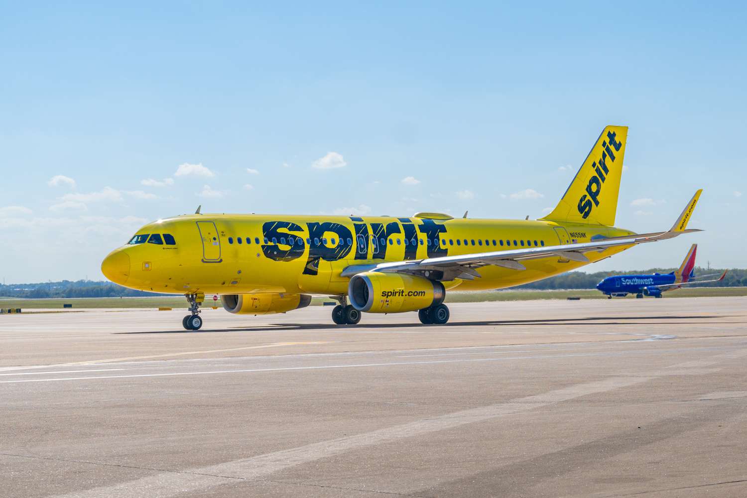 A yellow Spirit airlines plane is seen on a runway, with a blue Southwest plane in the background.
