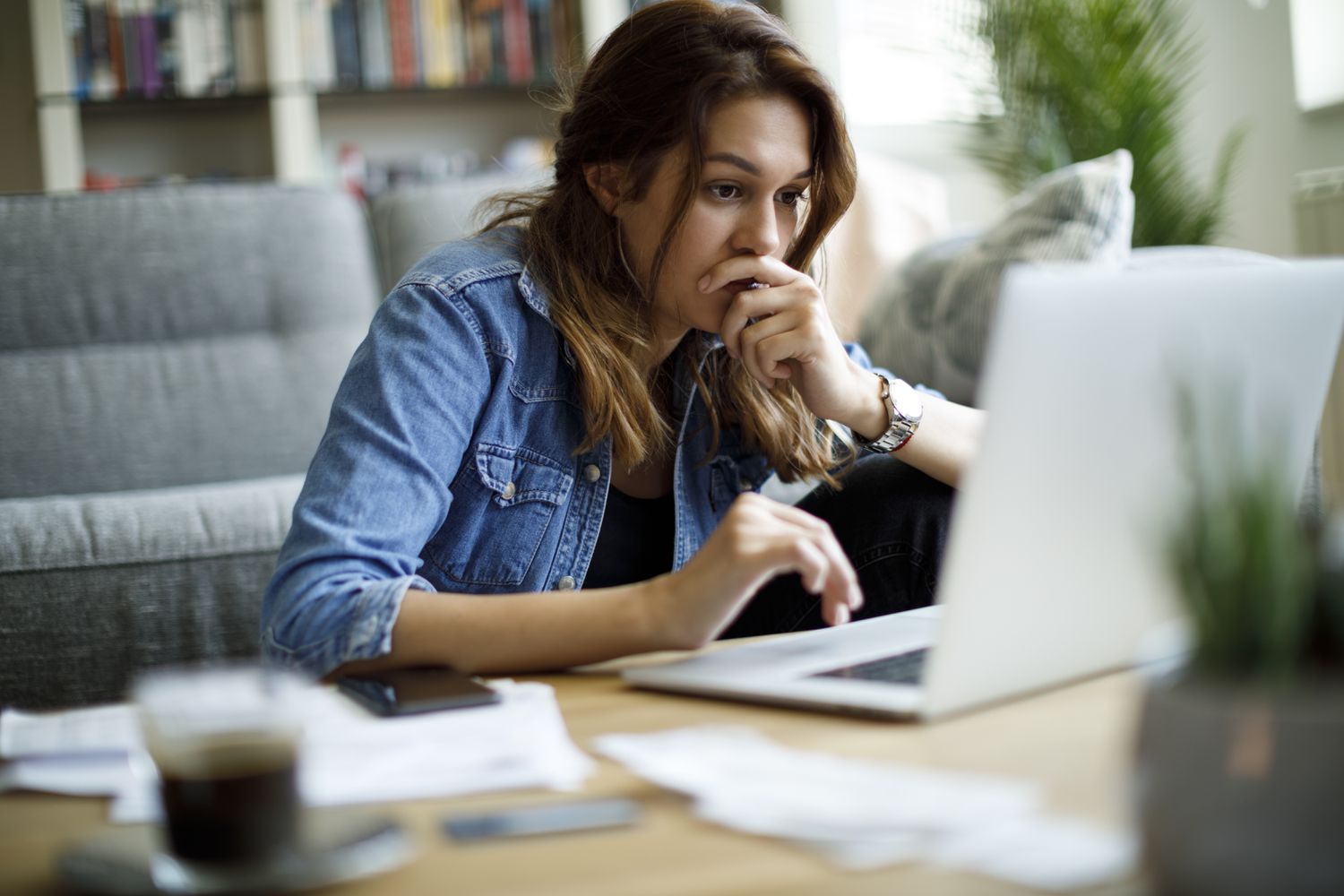 Worried young woman looking at bills on her laptop screen.