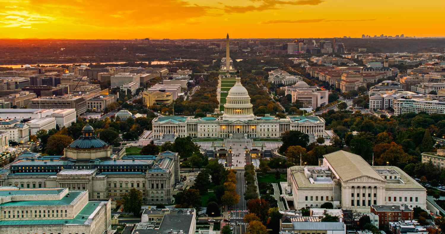 Helicopter shot of the United States Capitol and Supreme Court Building in Washington, D.C. at sunset, with the National Mall in the background.