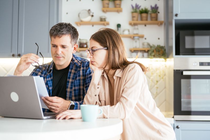 Couple in their 30s sitting in their kitchen and looking at bank CD rates on a laptop