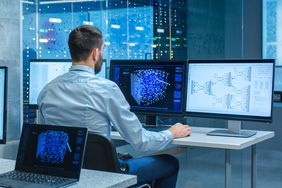 Computer engineer at workstation in office that is full of displays showing 3D representations of neural networks