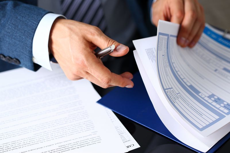 A registered broker-dealer holds a pen as they flip through paperwork looking for a particular SEC form.