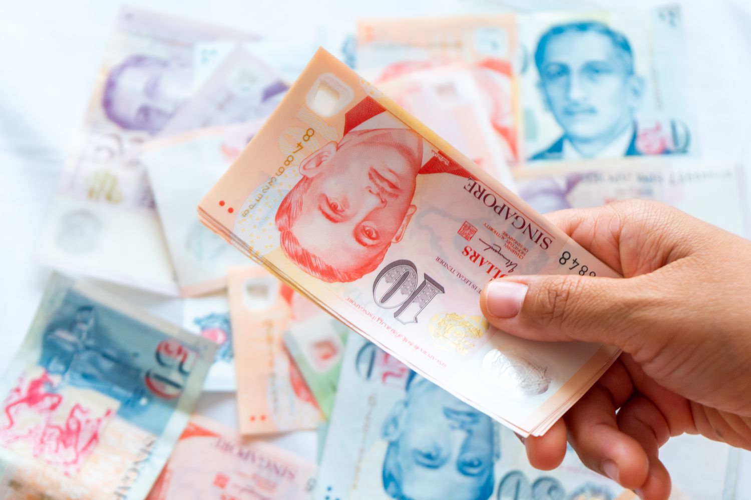 A hand holding a Singapore dollar banknote