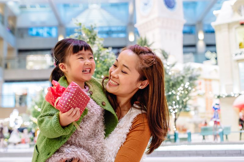A mom carrying her daughter, who's holding a wrapped present