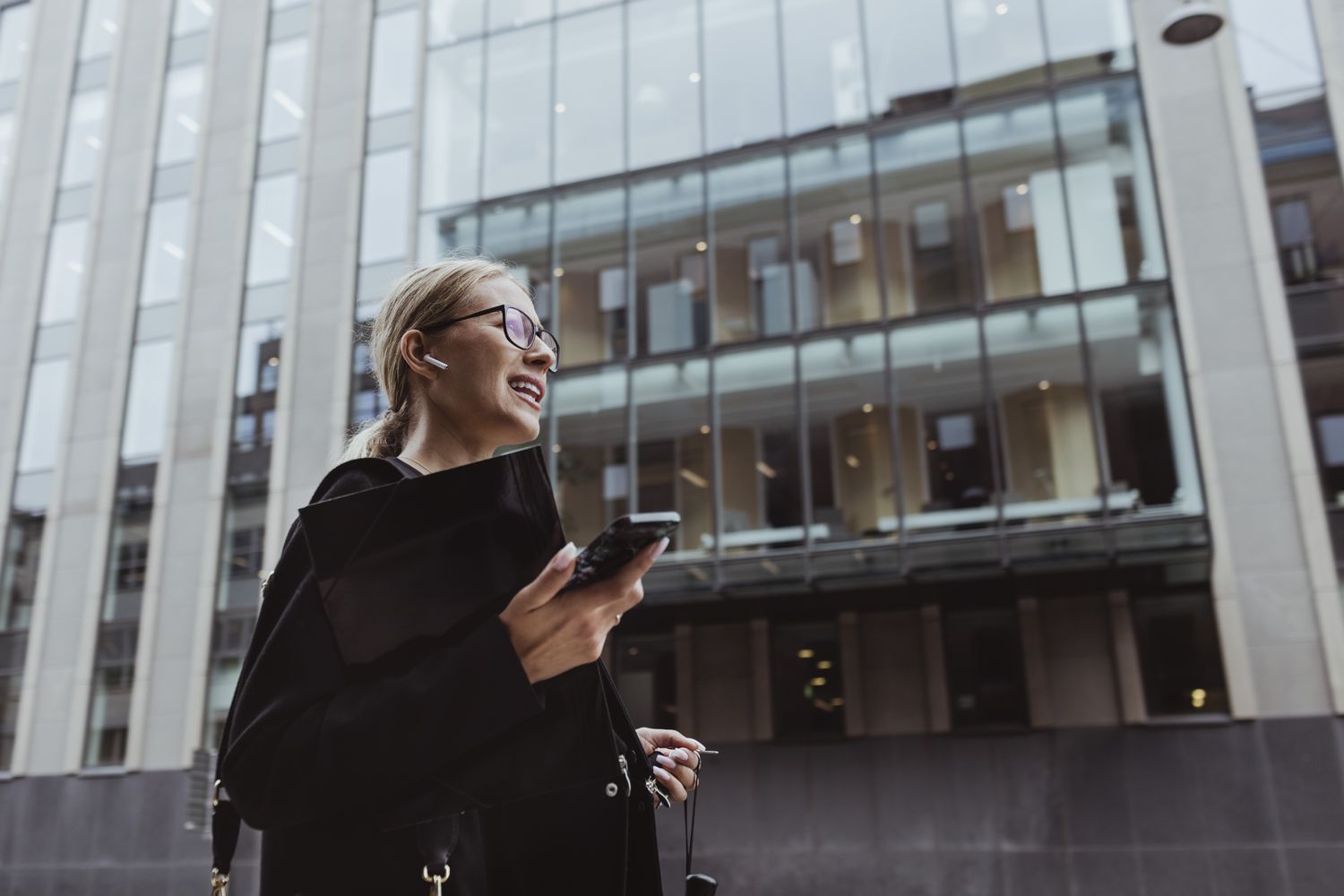 Businesswoman walking in the city surrounded by high-rises, with in-ear headphones on.