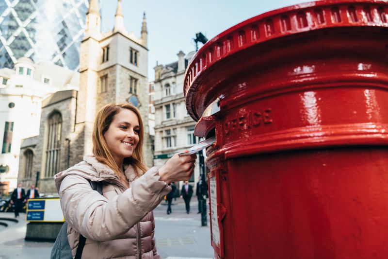 Woman posting a money order in an air mail envelope at a post box in London. 