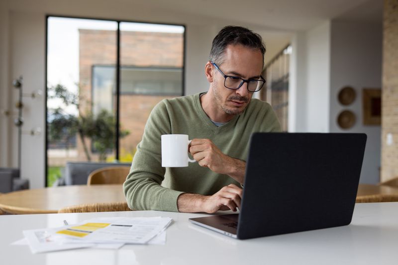 Man in his 40s or 50s, sitting at home and looking seriously at bank rates on his laptop