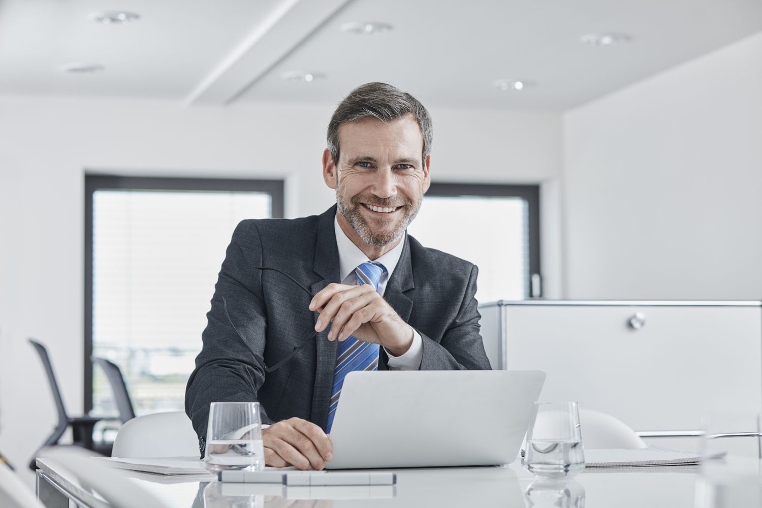 A smiling businessman with laptop at desk in office.