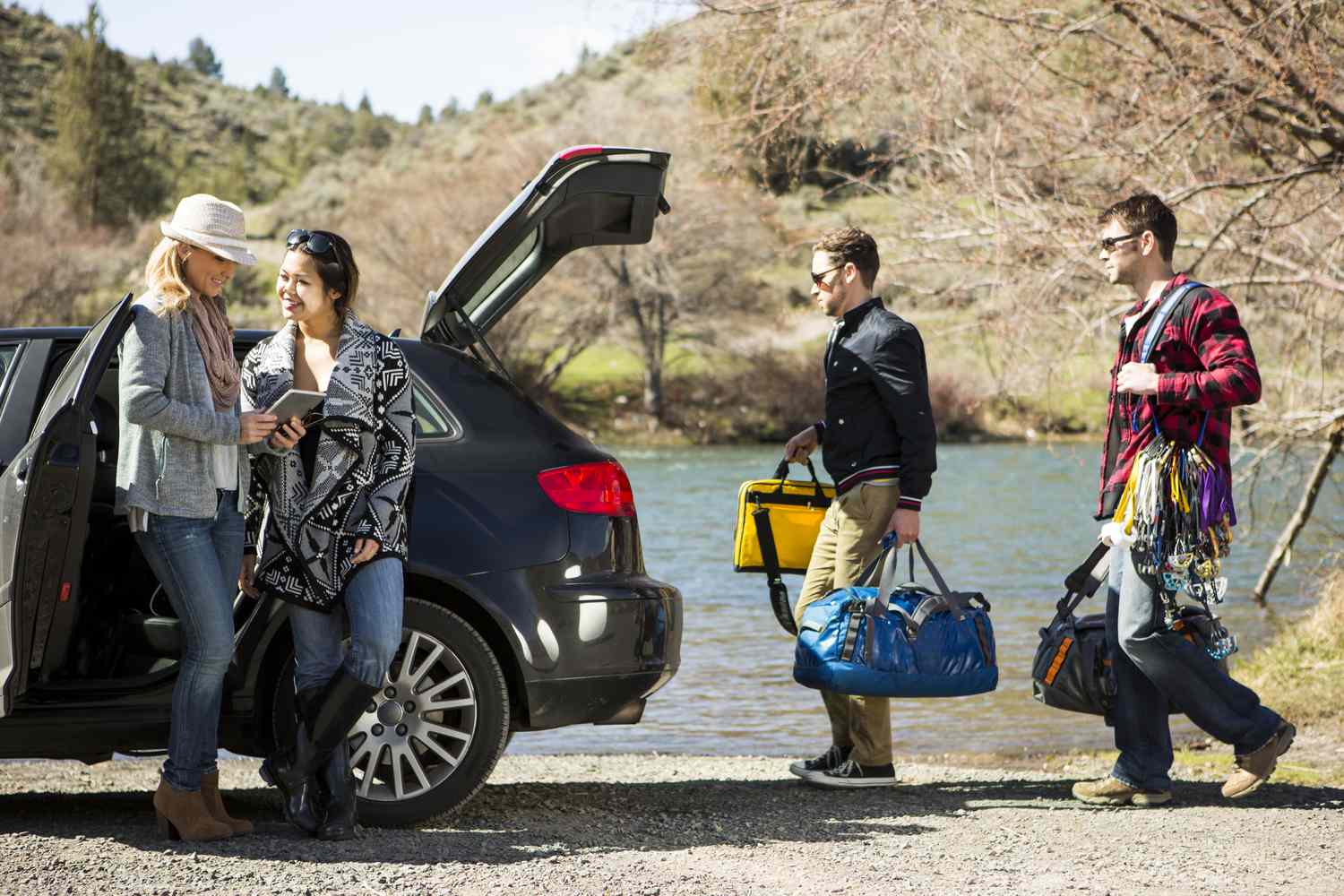 Two women using a digital table while two men load up a car for a road trip.