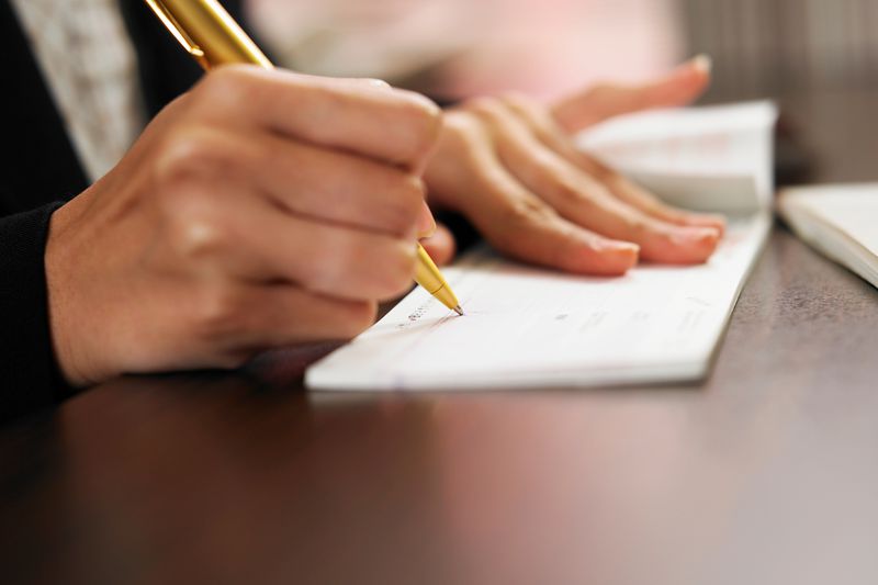 Cropped Hand Of Woman Signing On Check Over Table