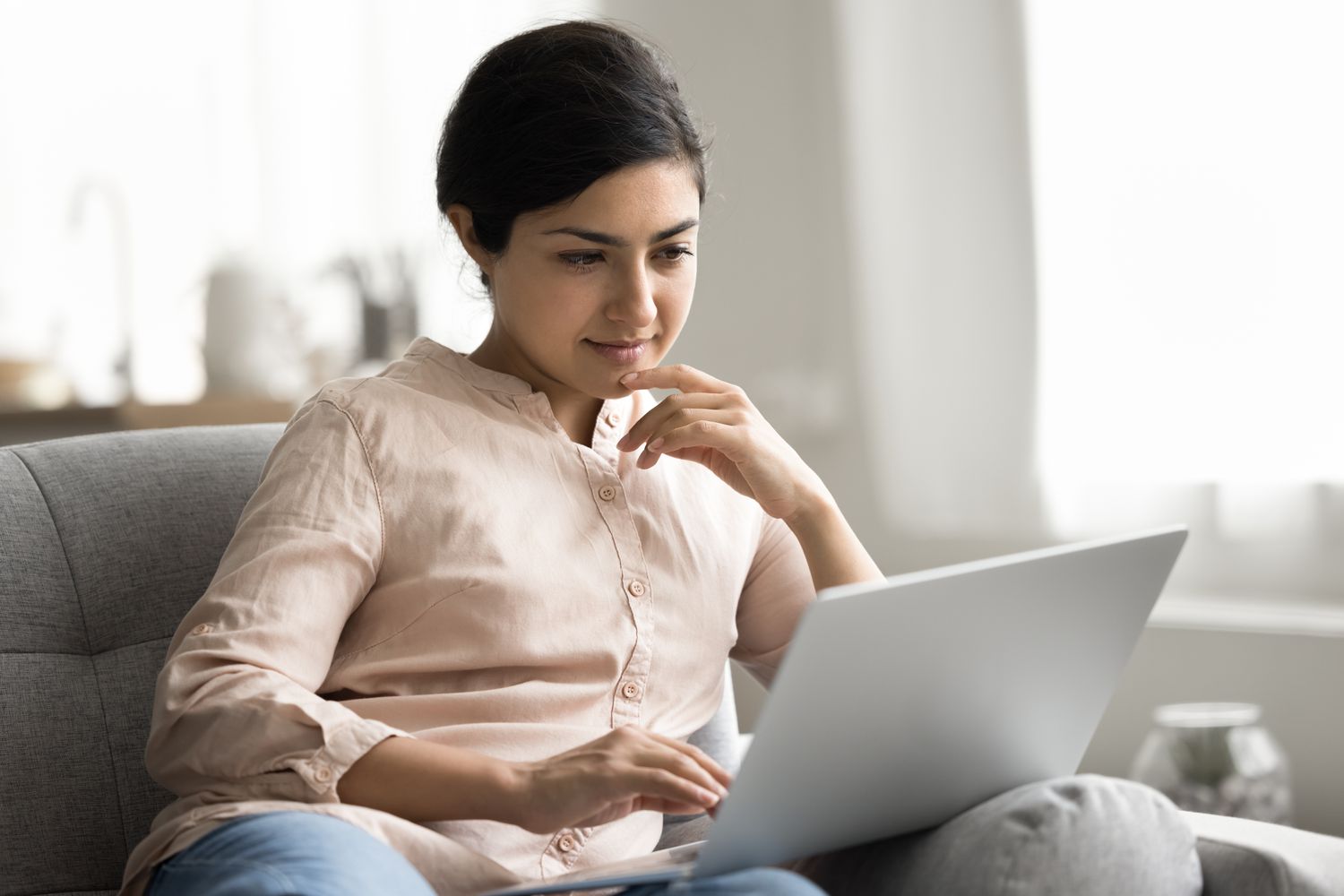 A woman sits on a couch with a laptop reading her screen