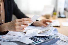 Hands holding receipts with more receipts, a calculator and glasses on the desk