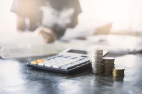 A close-up of calculator and coins with a person analyzing financial data.