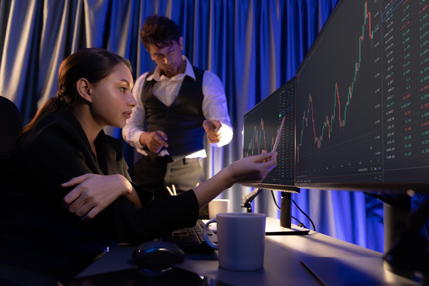 Woman in a darkened room looking at charts on multiple screens.