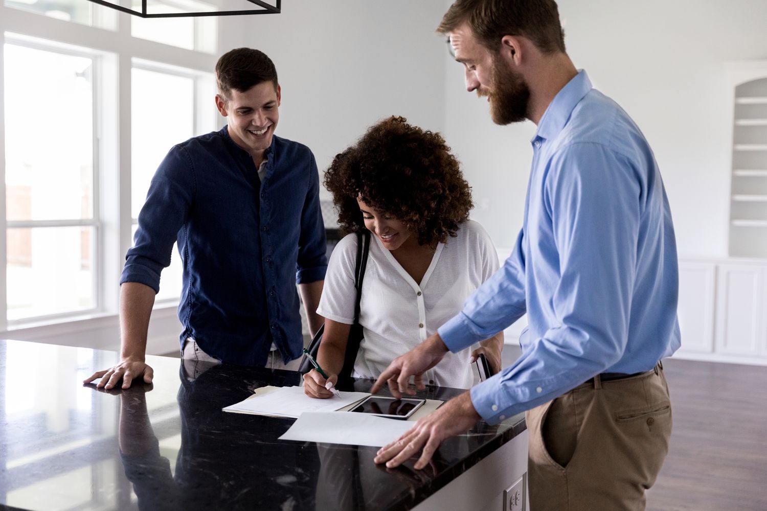 A real estate agent shows new homeowners where to sign on the closing documents. They are standing in an empty home.
