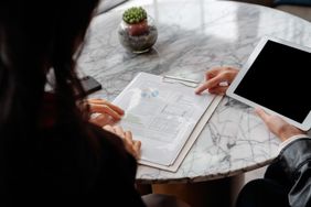 People discussing a balance sheet. One is holding a tablet while pointing to a document.