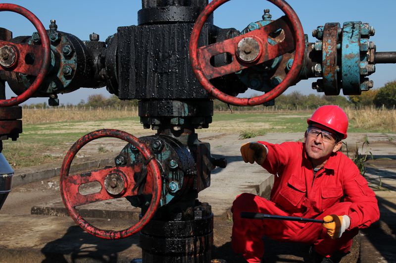 A wildcat oil worker uses a large wrench on an old oil drill head in hopes of extracting more crude oil.
