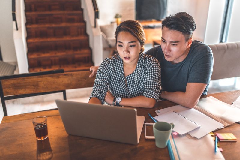 Serious young couple planning budget over laptop at table. 