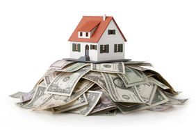 A miniature model house standing on a heap of dollar bills.