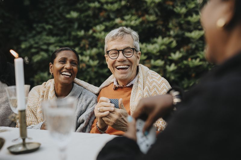 Senior man playing cards with family members at outdoor party.