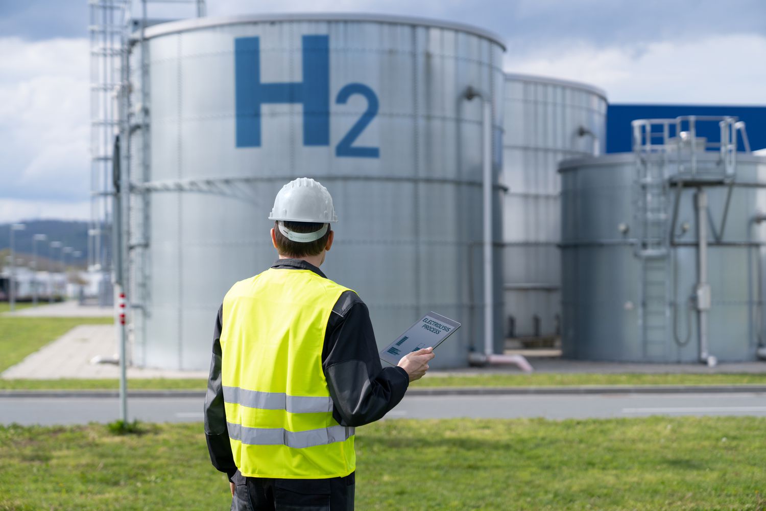 Engineer holding a tablet looking at hydrogen tanks in a hydrogen production facility.