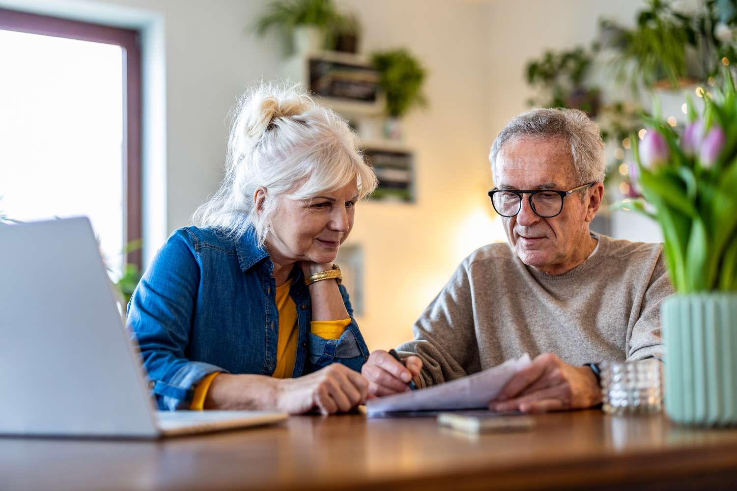 Older couple sitting at their dining room table and looking at financial statements and a laptop