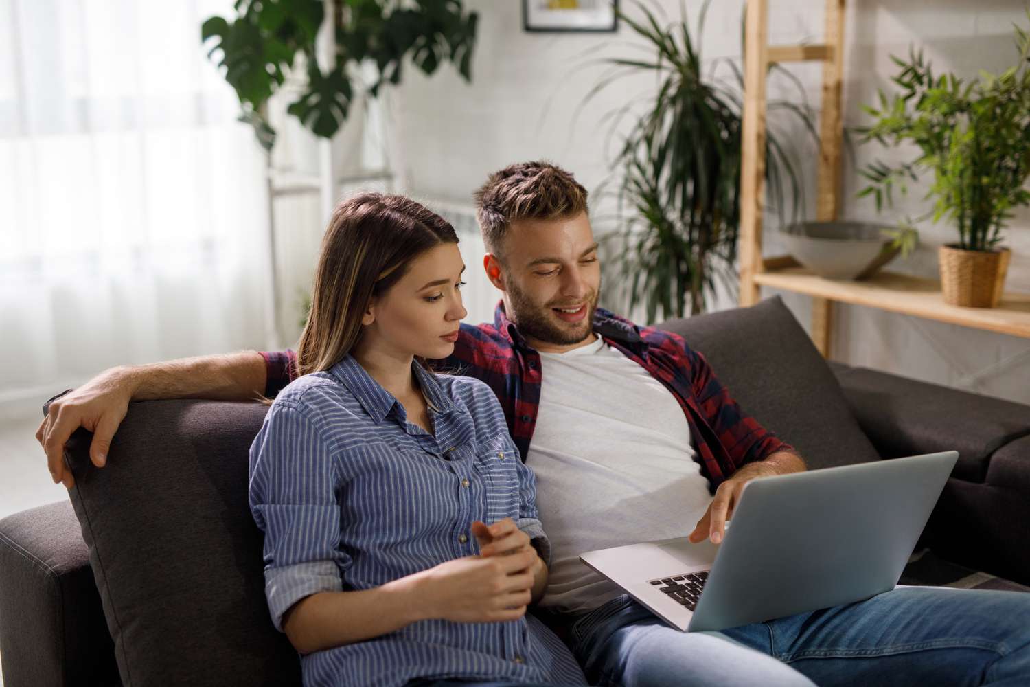 Young couple sitting on their living room couch and looking at something on a laptop