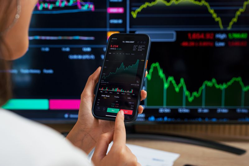 A woman holds a cell phone displaying stock information.