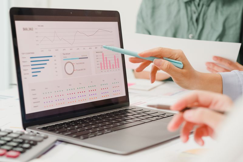 Closeup image of people sitting at a table, with one person pointing to charts on a laptop screen